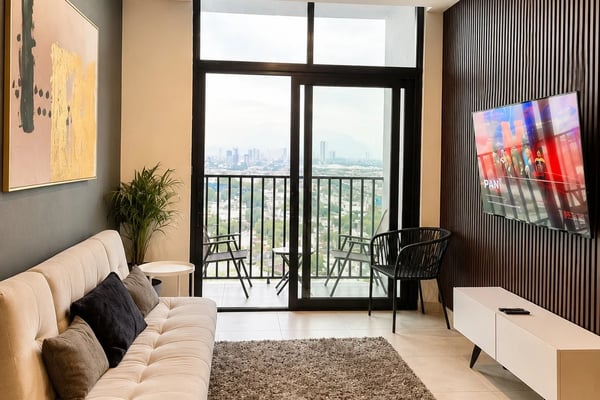 Sala moderna con sofá de cuero café, cojines coloridos y ventanas de piso a techo con vista a las montañas y luces de la ciudad al atardecer